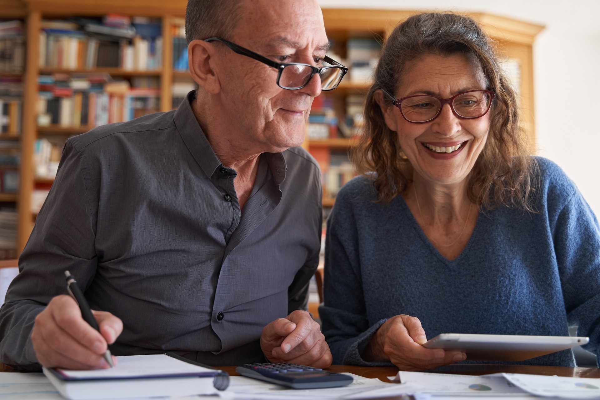 Senior couple with tablet and calculator smile while managing bills and paperwork. Domestic life budget