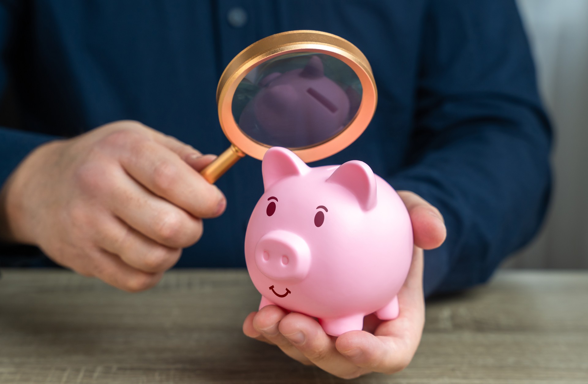 A man looks at a piggy bank with a magnifying glass. Investigating capital origins. Anti money laundering, tax evasion. Transparency and accountability. Study terms and conditions on deposit.